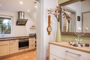 A modern kitchen with a built-in oven, a stainless steel range hood, and a window with a view of greenery.