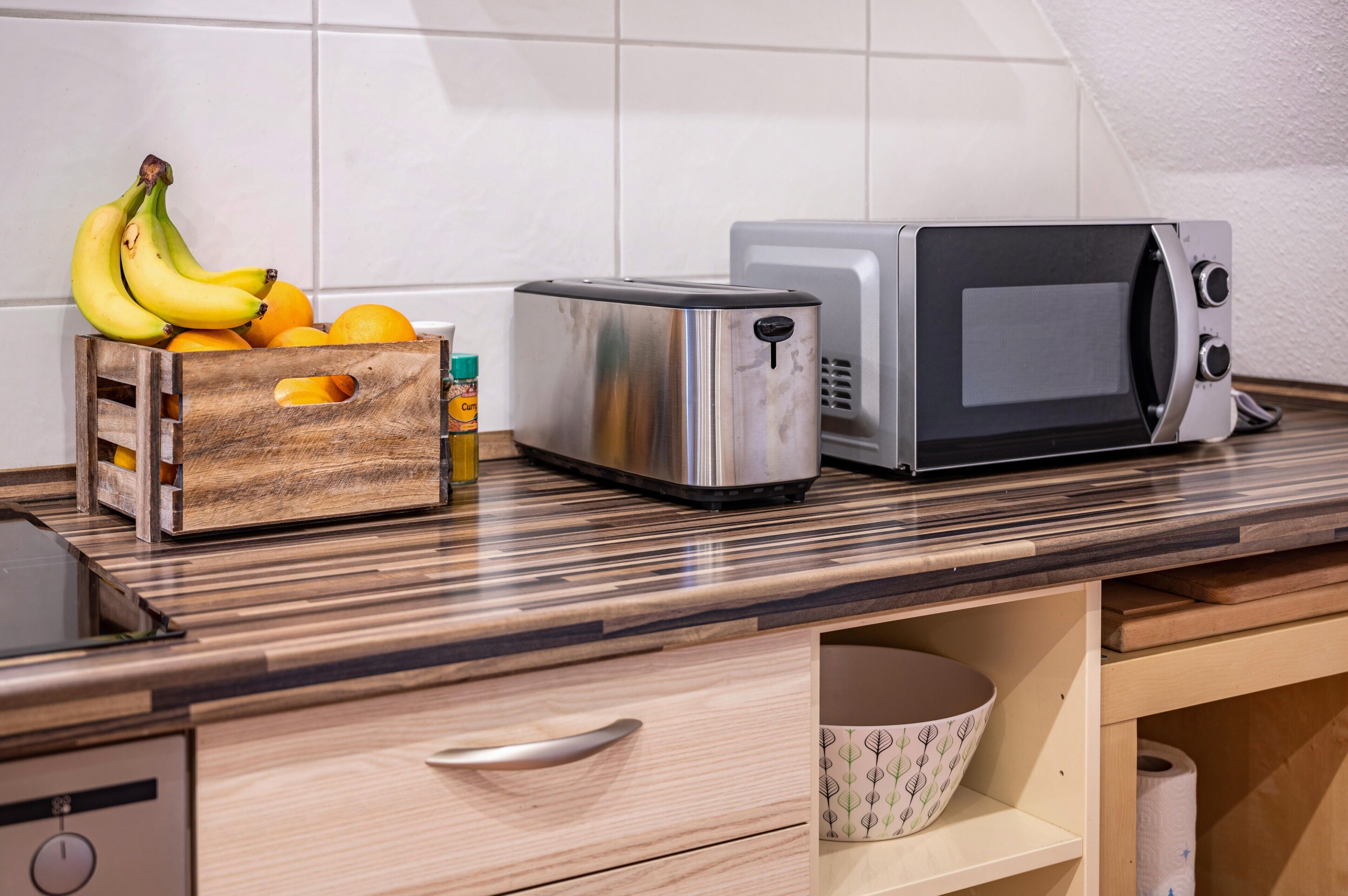 Eine Küche mit Toaster, Mikrowelle, einer Holzkiste mit Obst und einer Schüssel auf der Arbeitsfläche.