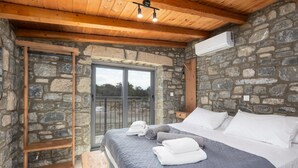 Une chambre avec un mur en pierre, un plafond en bois, un lit recouvert de draps blancs et une vue sur l’extérieur, visible à travers une porte vitrée.