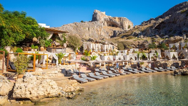 Un complexe hôtelier en bord de mer, doté de chaises longues, de parasols et offrant une vue sur un château historique.