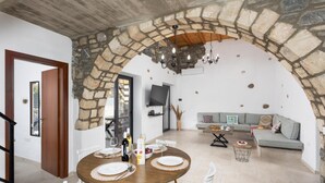 Un coin repas agrémenté d’une arche en pierre, d’une table en bois dressée pour quatre personnes et d’un canapé en arrière-plan.
