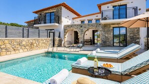 Un espace aménagé au bord de la piscine, avec des chaises longues, une table sur laquelle se trouvent une bouteille et des verres, et un mur en pierre.