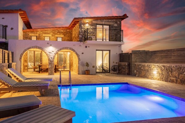 A two-story house with a swimming pool, stone walls, and outdoor seating.
