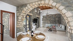 A dining area with a stone arch, a round table set for four, and a sofa in the background. - La Casa Di Pietre 3 in Rhodes (Rhodes)