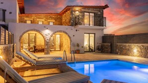 A poolside area with lounge chairs, a stone wall, and a balcony overlooking the pool. - La Casa Di Pietre 3 in Rhodes (Rhodes)
