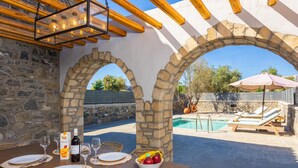 An outdoor dining area with stone arches, a pool, and lounge chairs. - La Casa Di Pietre 3 in Rhodes (Rhodes)