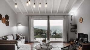 A modern living room with a sofa, a coffee table, and a TV. There is a balcony with a view of the sea. - Villa Gardenia in Paxi (Paxos)