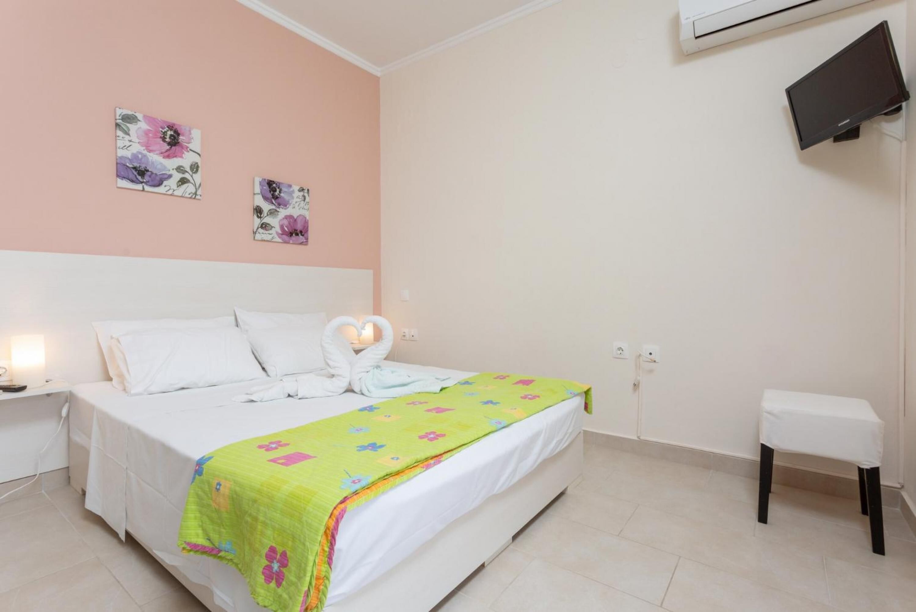 A bedroom with a bed, a bedside table, a nightstand, a TV mounted on the wall, and a small table by the bed.