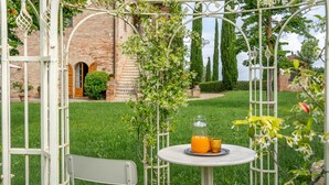 Ein Garten mit einem Ziegelgebäude, einer weißen Metallpergola und einem Tisch mit einem Glas Orangensaft.