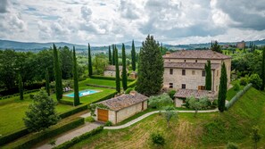 A large stone building with a swimming pool, surrounded by well-maintained gardens and tall trees. - Il Poggio Alle Trese 14 Emma Villas (Citta della Pieve)