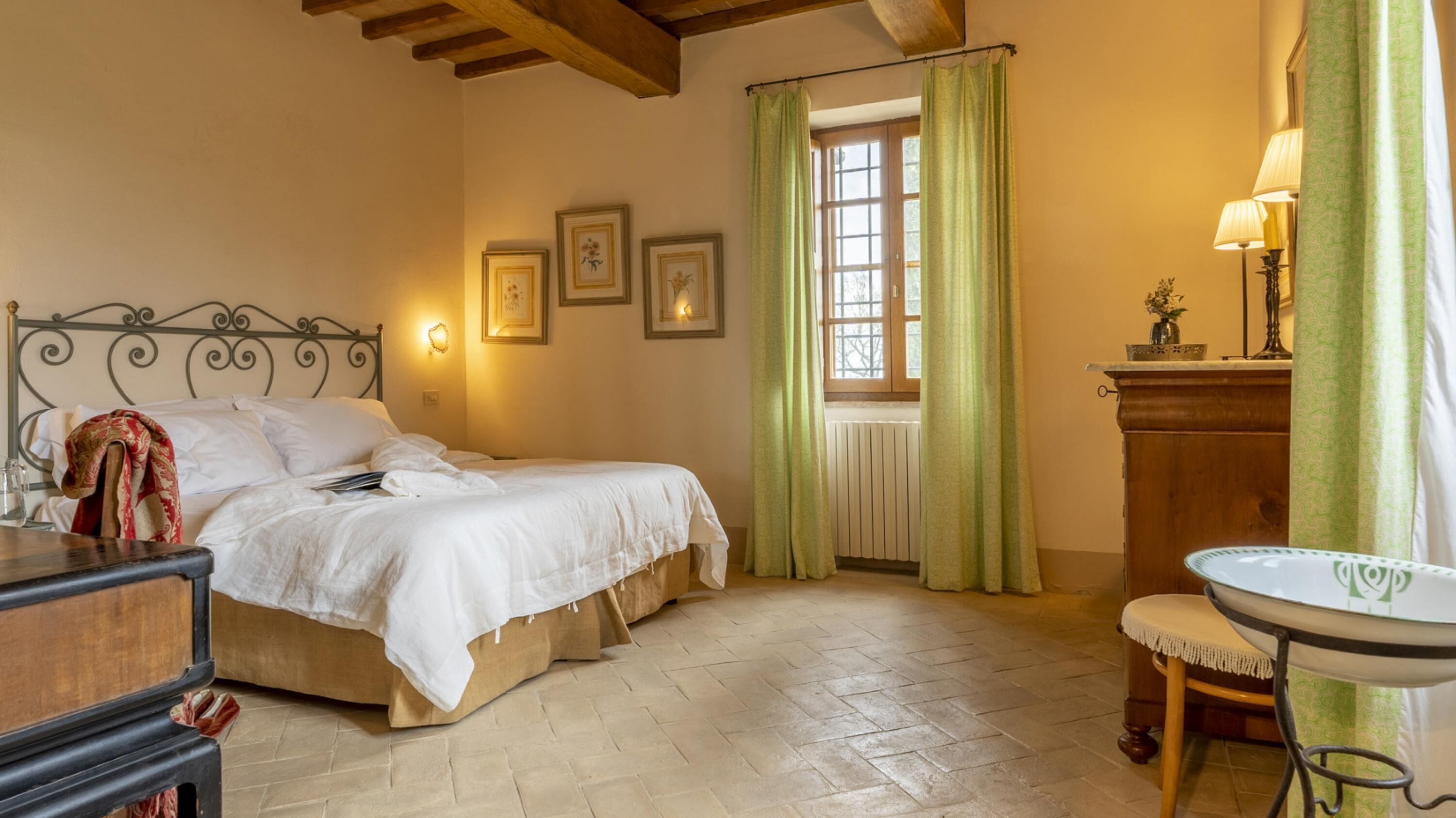 Un dormitorio con cama doble, mesita de noche, cómoda, ventana con cortinas y una pequeña mesa con lámpara.