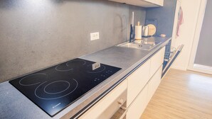 A modern kitchen with a black induction cooktop, a stainless steel sink, and a built-in oven. - Residenza Del Porto - Italian Homing (Padenghe sul Garda)
