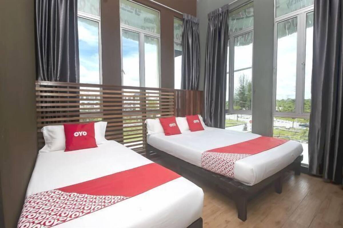 Two beds with red and white bedding, a wooden headboard, and a view through large windows.
