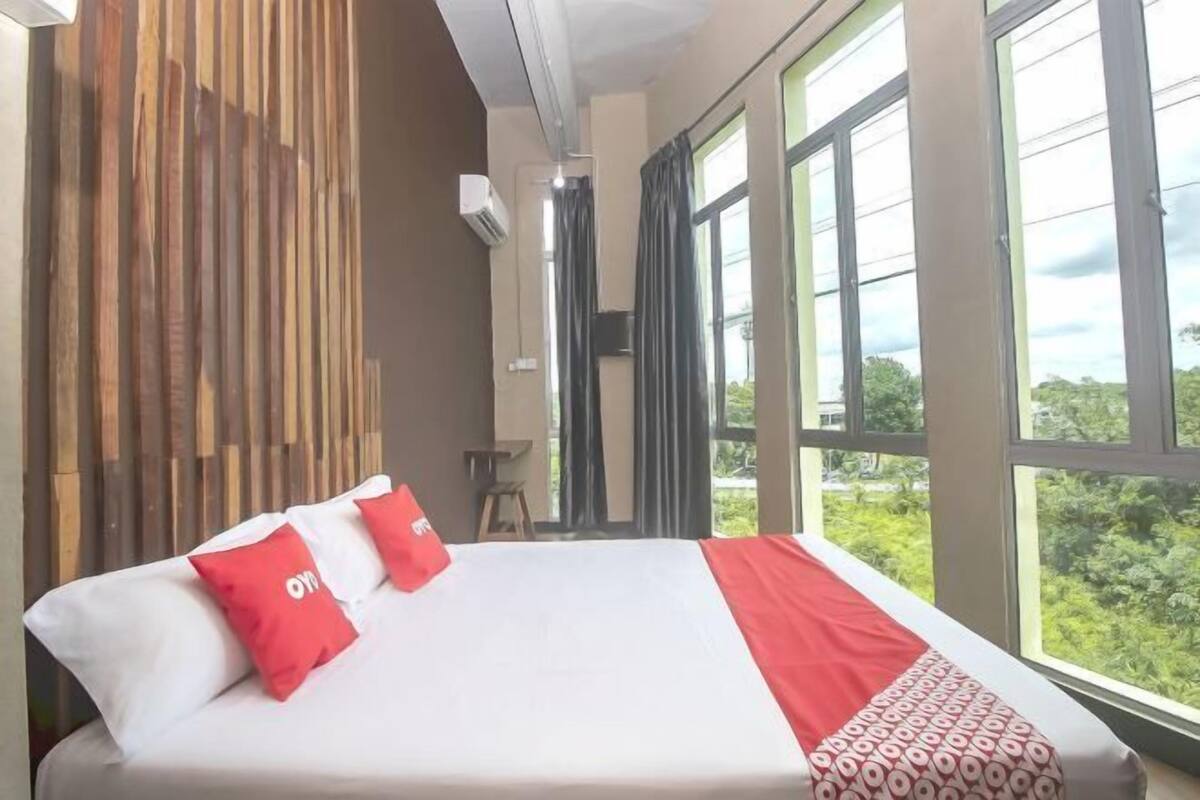 A hotel room with a bed, large windows, and a view of greenery.