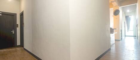 A hallway with a wooden floor, white walls, and a dark door on the left.