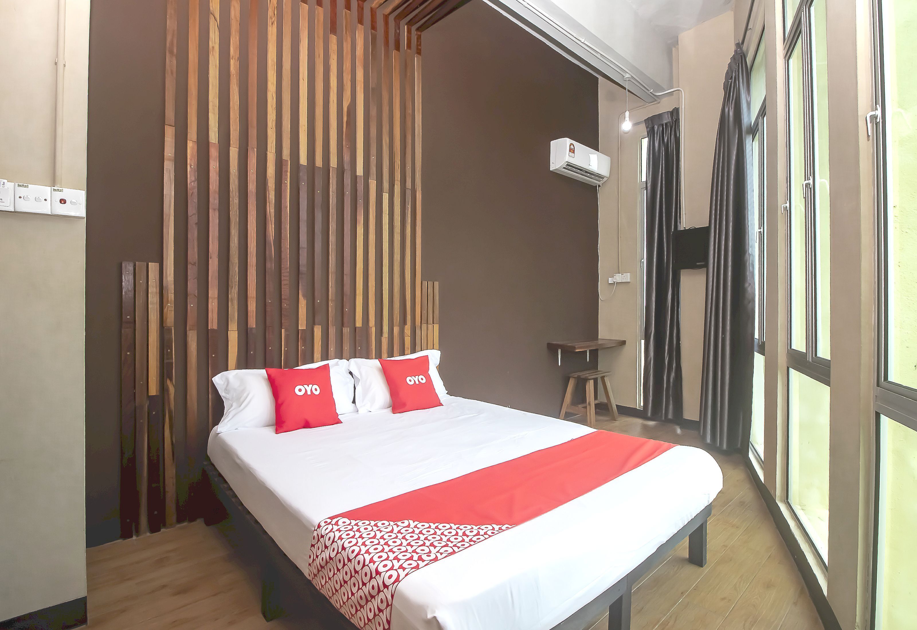 A hotel room with a bed, a wooden slat wall, an air conditioning unit, and a window with curtains.