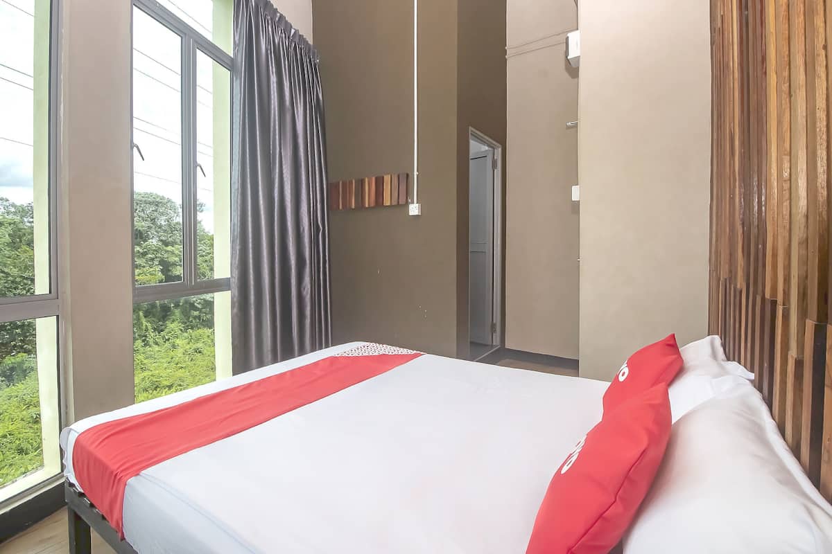 A hotel room with a large bed, a view of greenery outside, and a wooden headboard.