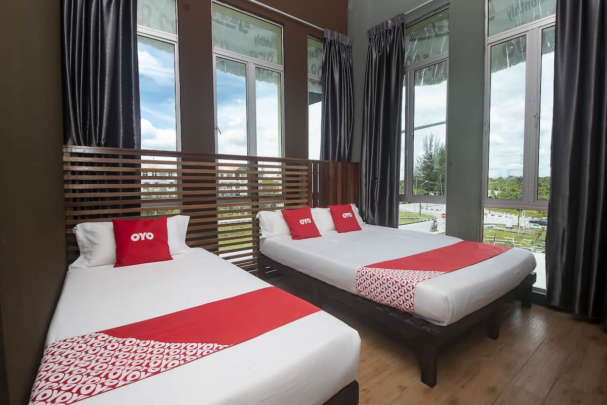 Two beds with white and red bedding, wooden headboards, and large windows with curtains.
