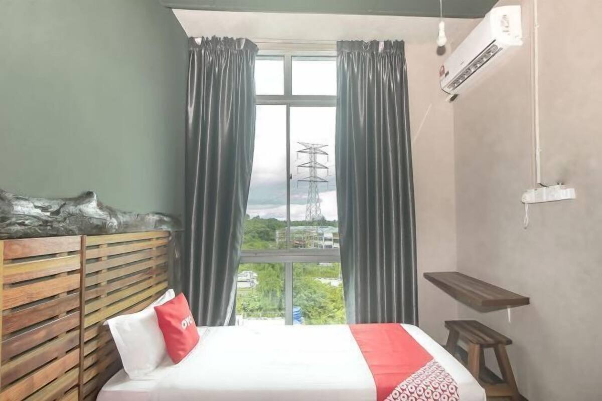 A hotel room with a bed, curtains, a wooden headboard, a small table, and an air conditioning unit.
