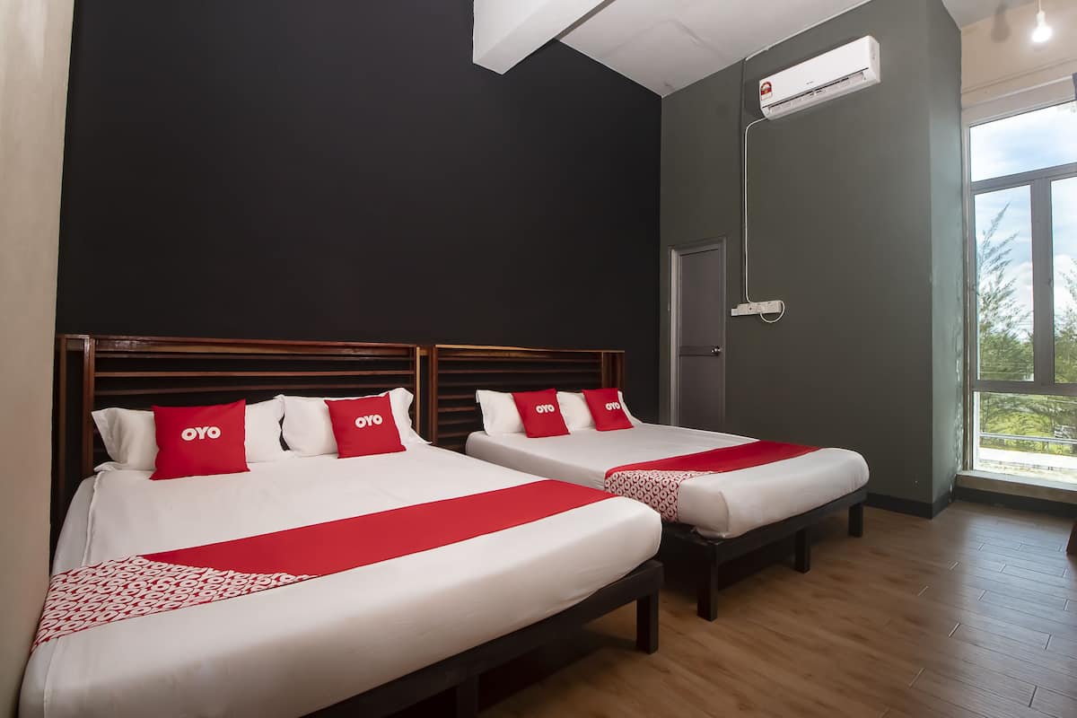A hotel room with two beds, each with a red and white bedspread and pillows, a wooden headboard, and a large window providing a view of greenery outside.