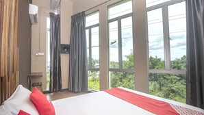 Ein Hotelzimmer mit einem großen Bett, einem Fernseher und einem Fenster mit Blick auf Grünflächen.