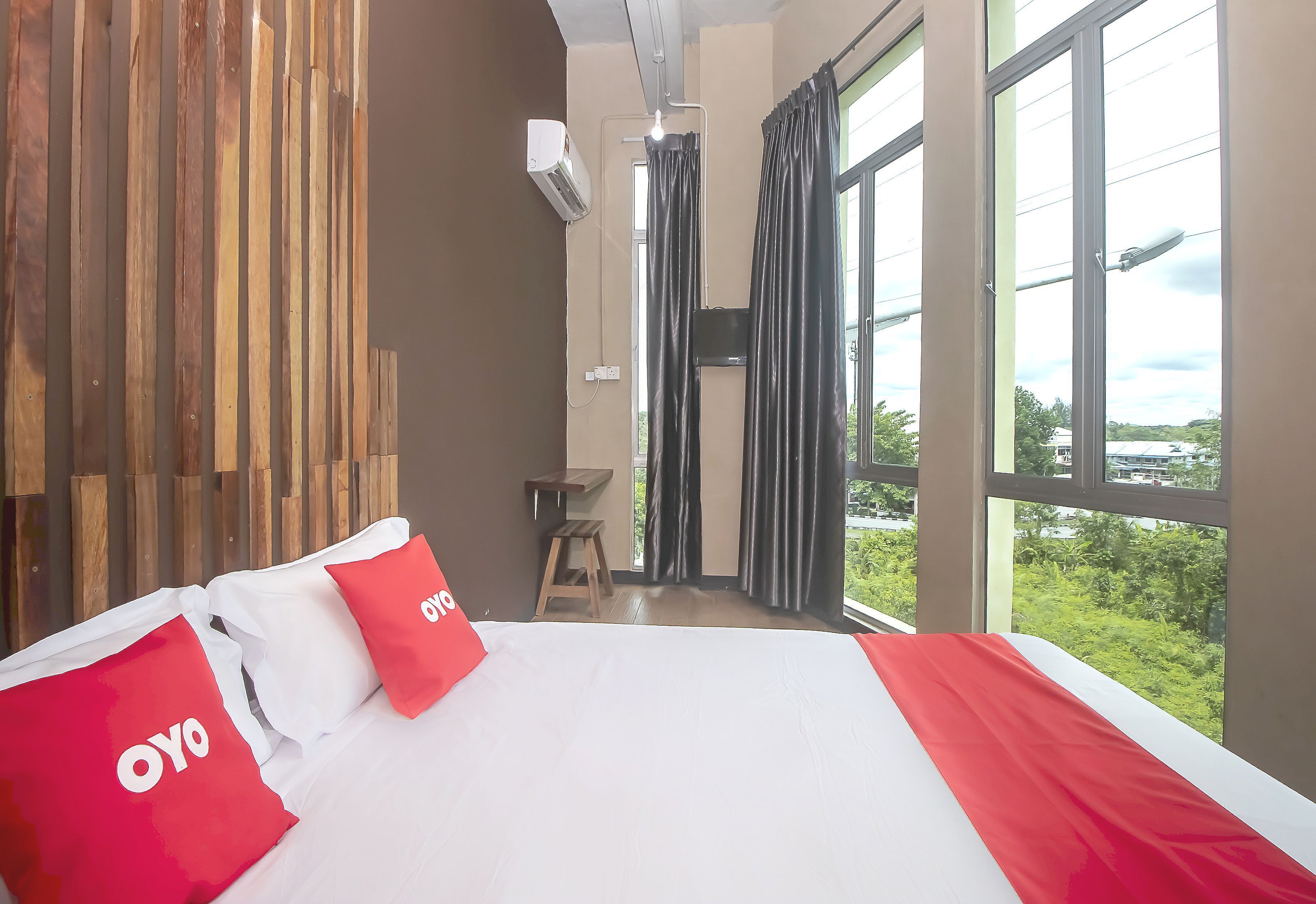 Habitación de hotel con una cama grande, un panel de pared de madera, una ventana con cortinas y vistas a zonas verdes.