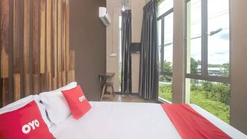 Habitación de hotel con una cama grande, un panel de pared de madera, una ventana con cortinas y vistas a zonas verdes.