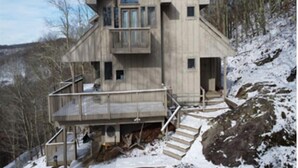 Eine Holzhütte mit Balkon, Treppe und Blick auf den umliegenden Wald.