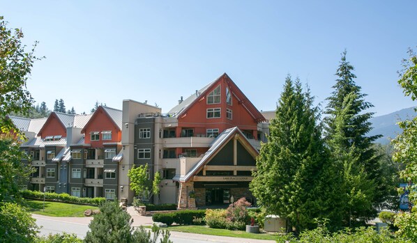 A multi-story lodge with a prominent red and grey facade, stone accents, and a well-maintained garden area.