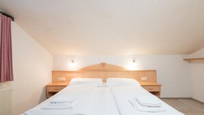 Un lit double avec du linge de lit blanc, deux tables de chevet, une tête de lit en bois et un luminaire au-dessus du lit.
