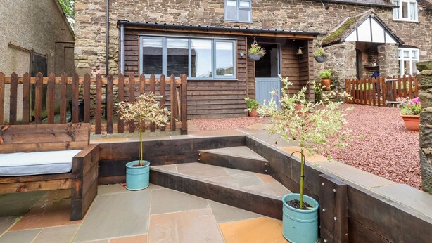 A stone house with a wooden fence, a front door, and steps leading to a porch. - The Brewhouse (Church Stretton)