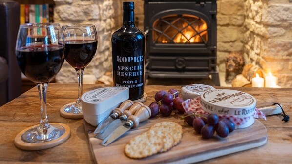 A wooden table with a bottle of port wine, two glasses of red wine, cheese, grapes, crackers, and a cheese knife. - Moorhens - Cotswold Water Park (Cotswold Water Park)