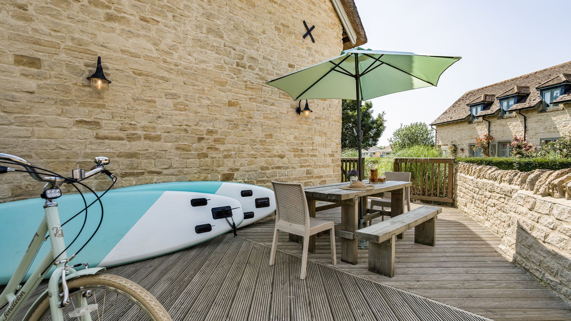 A wooden deck with a table and chairs, a bicycle, and a surfboard.