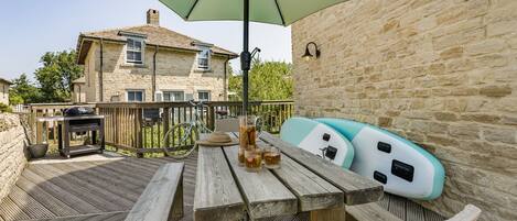 Une terrasse extérieure avec une table en bois, un barbecue et des kayaks gonflables.