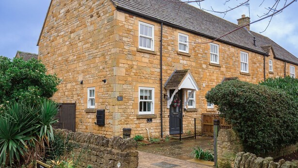 A stone building with a central entrance, multiple windows, and a small garden area with plants and a stone wall.