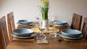A dining table set with blue plates, clear wine glasses, and a vase with yellow flowers.