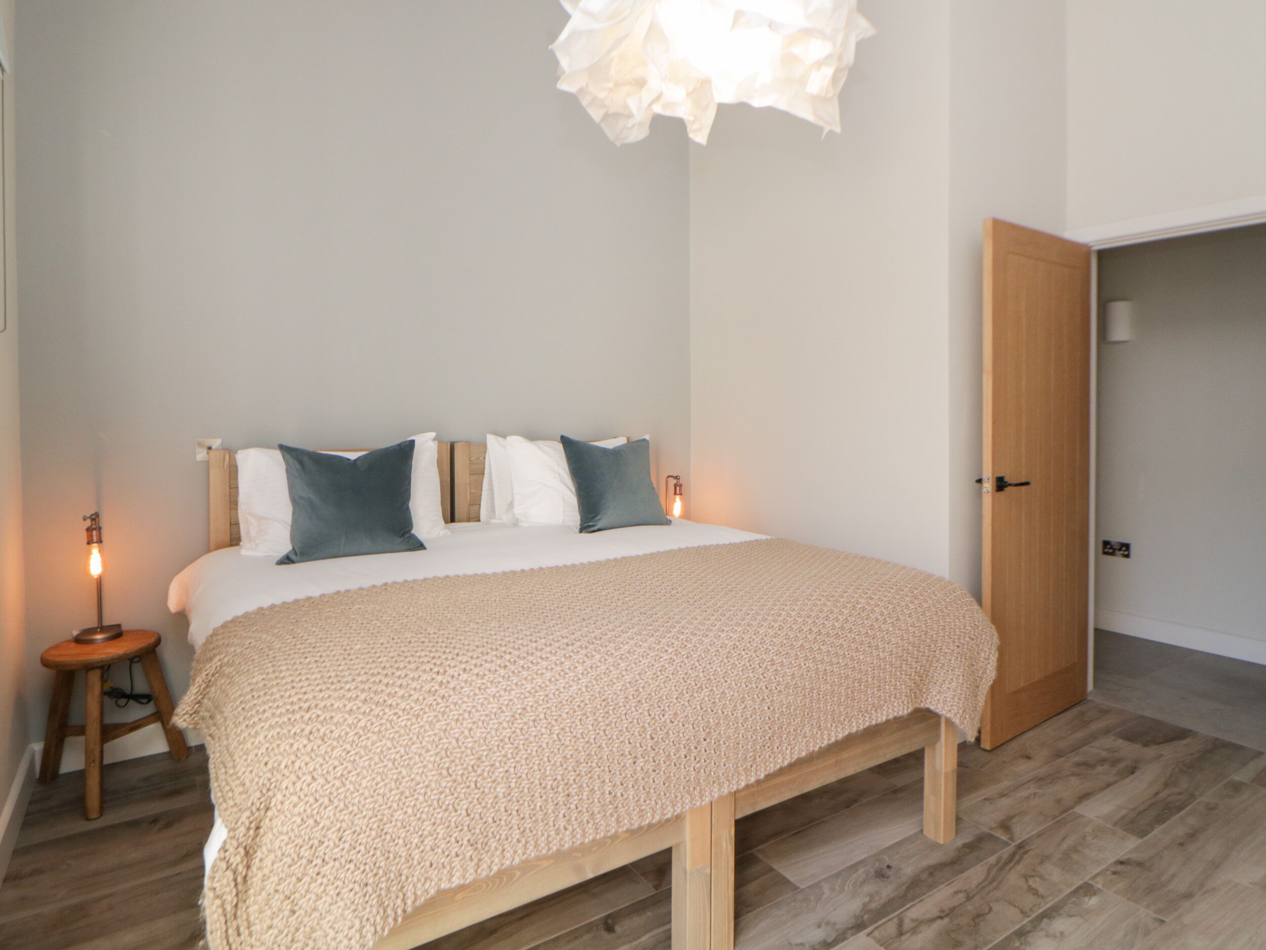 A bedroom with a bed, bedside lamps, a wooden floor, and a door.