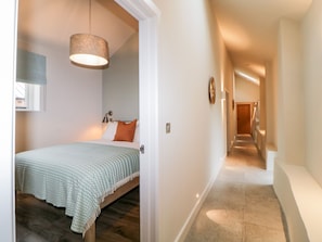 Ein Hotelzimmer mit Bett, einer Hängelampe, Holzboden und einem zur Tür führenden Gang.