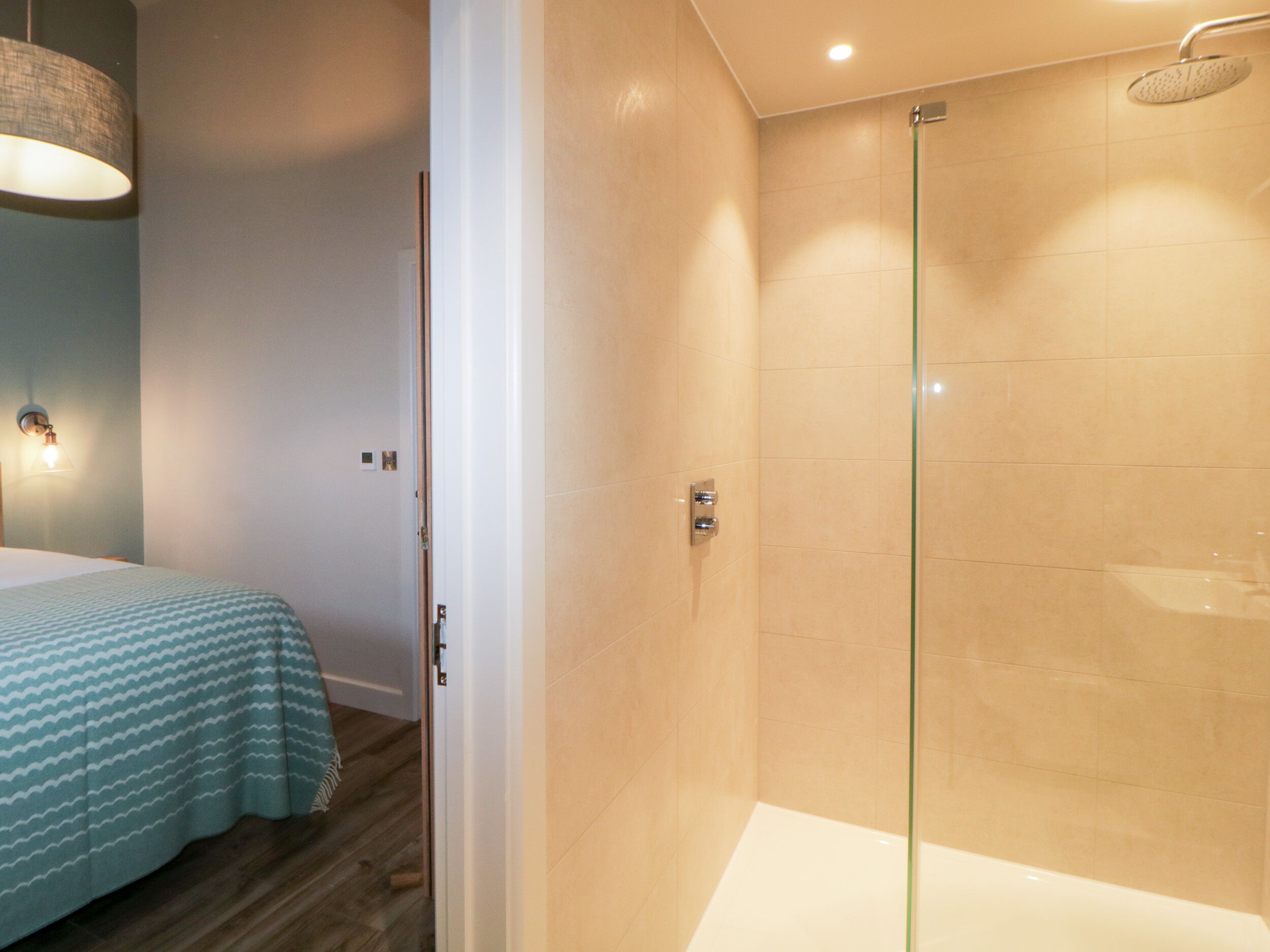 A modern bathroom with a glass shower enclosure, a bathtub, and a bed with a patterned bedspread.