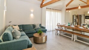 En moderne stue med en sofa, et spisebord dækket til fire personer, og et køkkenområde kan ses i baggrunden.