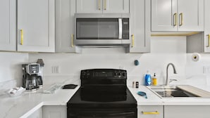 A modern kitchen with white cabinets, a black stove, a microwave, a coffee maker, and a sink. - La living bungalow with patio.  (Los Angeles)