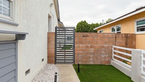 A gated property with a brick wall, a white fence, and a well-maintained lawn. - La living bungalow with patio.  (Los Angeles)