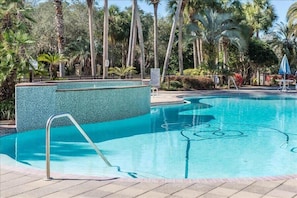 A swimming pool with a tiled edge, surrounded by palm trees and a clear blue sky.
