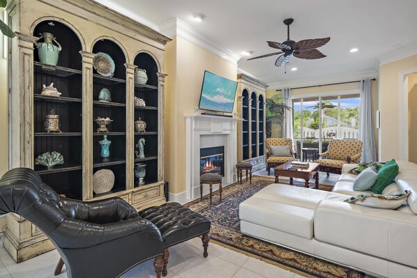 A living room with a fireplace, leather armchair, white sofa, and a bookshelf with decorative items.