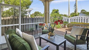 A covered patio area with a seating arrangement, including a sofa and chairs, a table, and a potted plant with flowers. - Golf Cart & 4 Bikes! 3 Min Walk to Pool & Hot Tub! 8 Min to Beach! New Listing! ~ Sunshine Retreat at Destiny West (Destin)