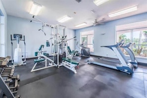 Une salle de sport équipée de matériel d’exercice, d’un tapis de course et de grandes fenêtres.