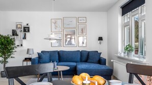 A modern living room with a blue sofa, a dining table with plates and candles, and a window with a view of greenery. - "Yorick" - 300m from the sea by Interhome (Skagen)