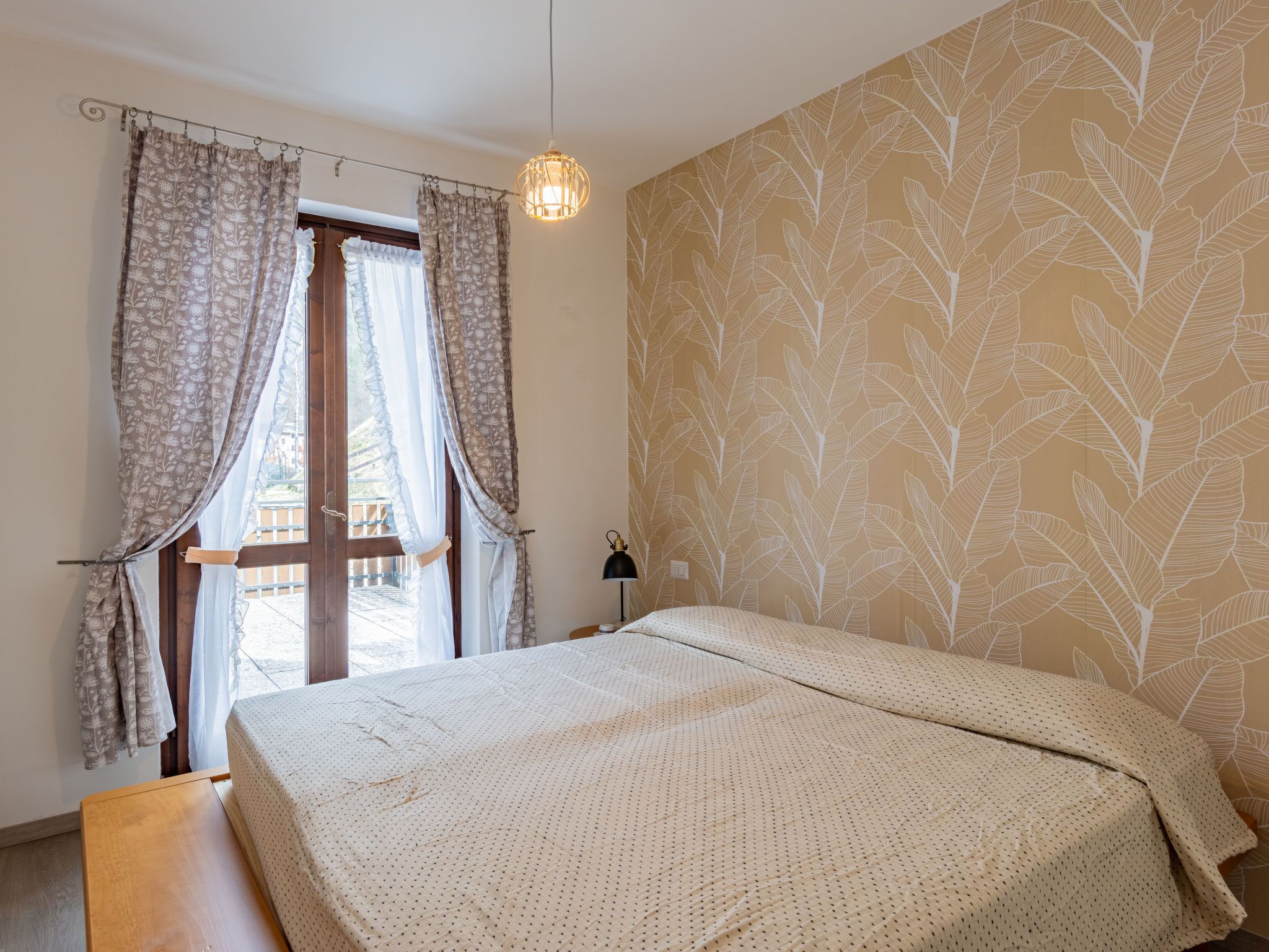 Una camera da letto con un letto, tende, un comodino, una lampada e una finestra con vista.