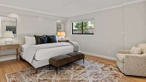 Une chambre à coucher comprenant un lit, des tables de chevet, un banc, une chaise et une fenêtre.