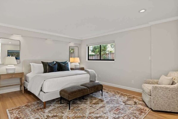 A bedroom with a bed, bedside tables, a bench, a chair, and a window.
